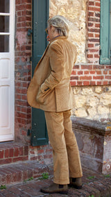 Fanny, vu de dos, sur la pas de la porte d'une maison à Trouville porte le costume droit unisexe Wes en velours côtelé couleur noisette de la collection Automne Hiver 2024 de la Maison Gabriel Paris