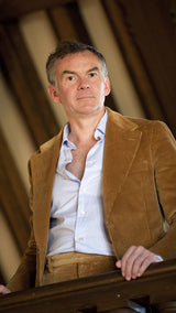 Cyril debout sur la mezzanine d'une maison à Trouville porte le costume droit unisexe Wes en velours côtelé couleur noisette de la collection Automne Hiver 2024 de la Maison Gabriel Paris