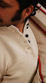Titouan allongé sur le canapé de la boutique Maison Gabriel Paris porte le pull marin Erwann en laine blanc cassé LE MINOR - détail boutonnage sur l'épaule - Collection Automne Hiver 2025 - Maison Gabriel Paris
