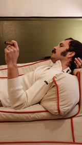 Titouan allongé sur le canapé de la boutique Maison Gabriel Paris fume un cigare et porte le pull marin Erwann en laine blanc cassé LE MINOR - Collection Automne Hiver 2025 - Maison Gabriel Paris