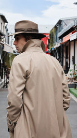 Pablo Saavedra de Decker aux Puces de Saint Ouen, de dos, porte le manteau raglan Hadrien en coton coloris mastic de la Maison Gabriel Paris