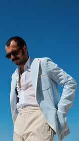 Titouan aux Tuileries avec un ciel bleu azur porte la veste James en seersucker à rayures bleu ciel et blanc galonnée - Collection Printemps été 2025 - Maison Gabriel Paris