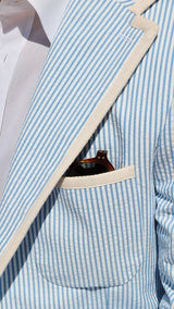 Titouan aux Tuileries porte la veste James en seersucker à rayures bleu ciel et blanc galonnée - détail de la poche et du col - Collection Printemps été 2025 - Maison Gabriel Paris