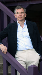 Cyril dans le jardin d'une maison à Trouville porte la veste droite Albert en en bouclette de laine noire de la collection Automne Hiver 2024 Maison Gabriel Paris