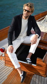Rein sur un voilier porte le blazer Ripley en laine natté bleu marine et le pull Tom col rond en laine mérinos blanc de la collection Plein Soleil de la Maison Gabriel Paris