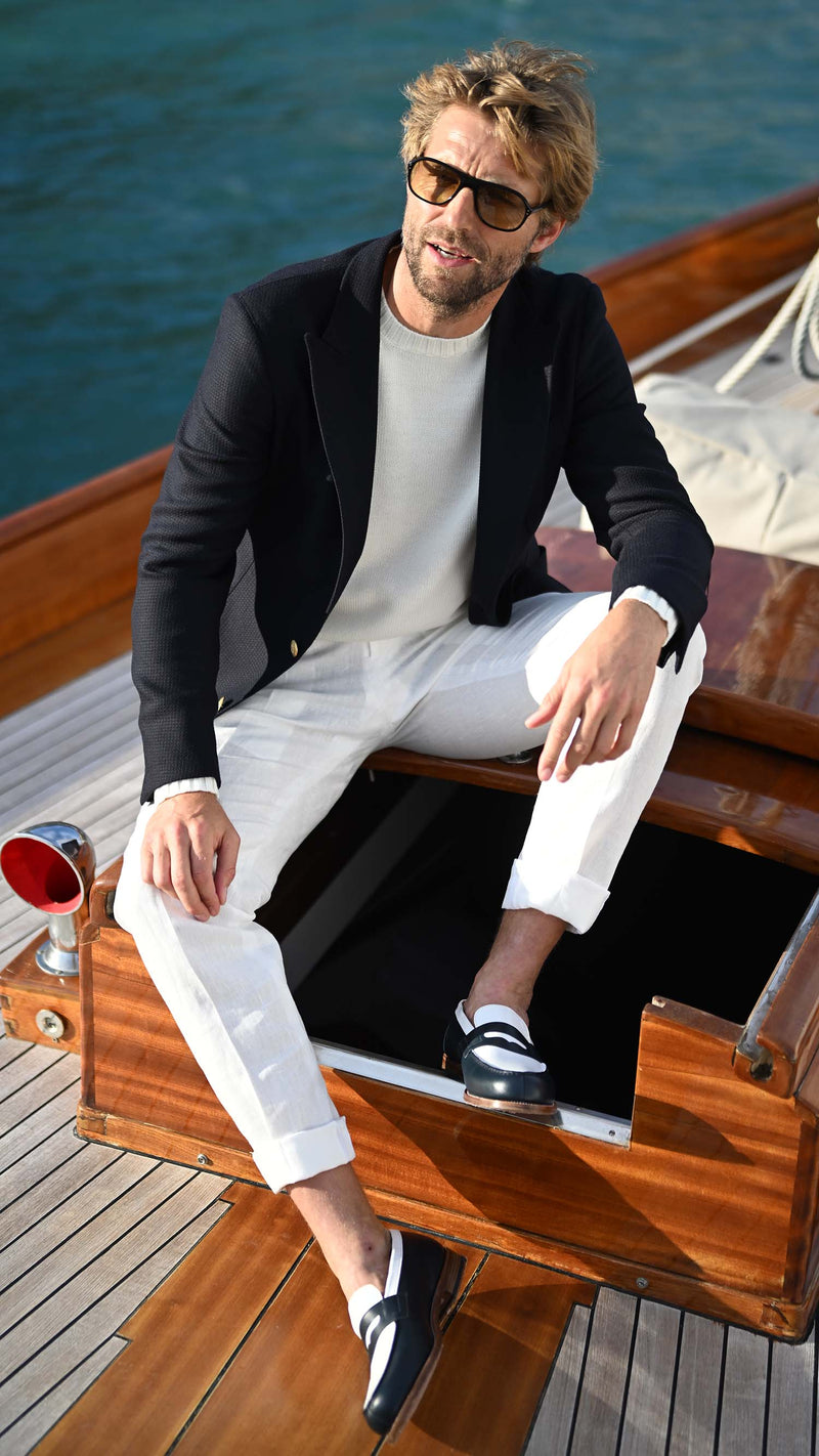 Rein sur un voilier porte le blazer Ripley en laine natté bleu marine et le pull Tom col rond en laine mérinos blanc de la collection Plein Soleil de la Maison Gabriel Paris