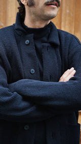 Titouan sur le pas de porte de la boutique Maison Gabriel Paris porte le cardigan Ayden en laine bleu marine LE MINOR X GABRIEL - zoom sur détail - Collection Automne Hiver 2025 - Maison Gabriel Paris