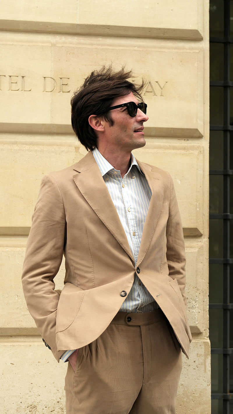 Devant l'Hôtel de Harley, Guillaume porte le costume Charly en milleraies d'été beige de la Maison Gabriel Paris - UNISEXE