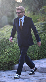 Rein marche à l'extérieur et porte le costume droit Louis en velours côtelé bleu, chaussé de ses mocassins bicolore J.M. Weston X Gabriel de la Maison Gabriel Paris