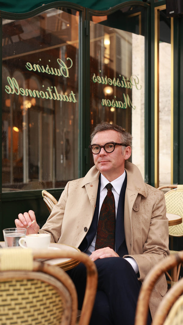 Cyril assis à la terrasse du Café de l'Epoque porte la cravate Florence en laine et soie motif cachemire bleu, jaune, rouge et vert de la collection André Malraux par la Maison Gabriel Paris
