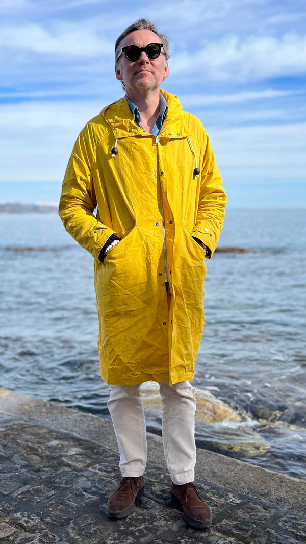 Cyril sur la jetée de Saint-Tropez porte le manteau de pluie Jean-Louis en wax jaune - au bord de l'eau - de la Maison Gabriel Paris