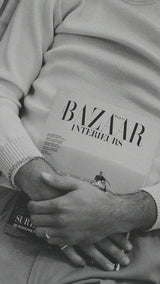 Titouan allongé sur le canapé de la boutique Maison Gabriel Paris prend la pose avec le magazine Bazaar Intérieurs et porte le pull marin Erwann en laine blanc cassé LE MINOR - Collection Automne Hiver 2025 - Maison Gabriel Paris