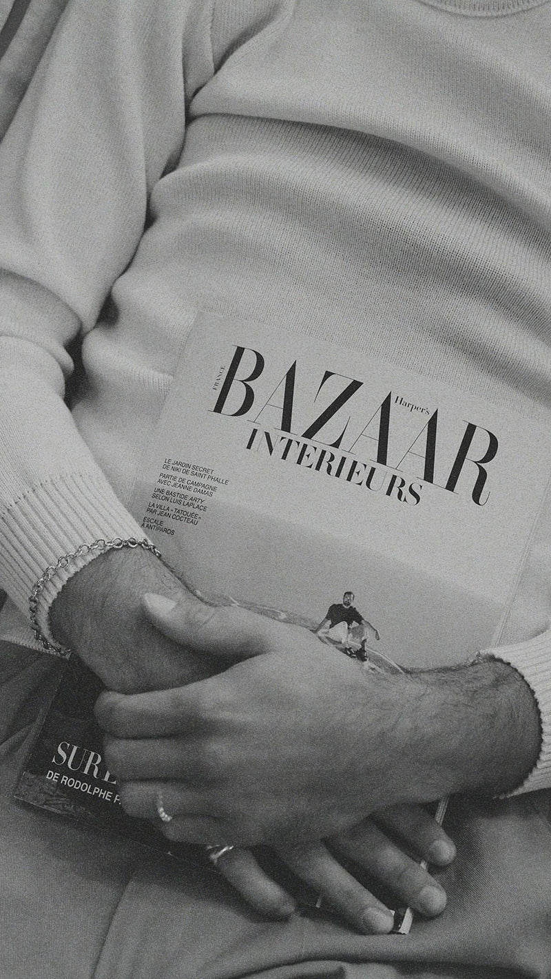 Titouan allongé sur le canapé de la boutique Maison Gabriel Paris prend la pose avec le magazine Bazaar Intérieurs et porte le pull marin Erwann en laine blanc cassé LE MINOR - Collection Automne Hiver 2025 - Maison Gabriel Paris