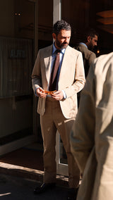 Élie porte le costume droit Raphel en lin et coton coloris mastic - photographié devant le restaurant parisien Alfi's - Collection Printemps-Été 2025 - Maison Gabriel Paris